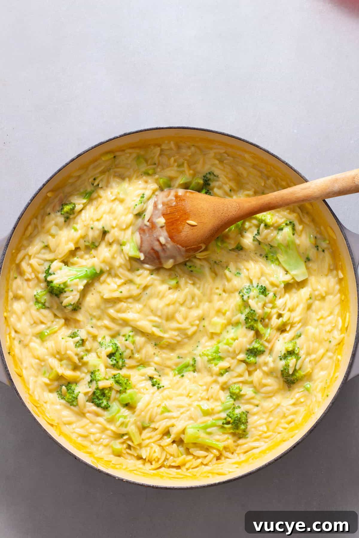 Creamy Broccoli Orzo Pasta with Garlic and Parmesan 11 A wooden spoon finishing a large skillet of creamy broccoli orzo.