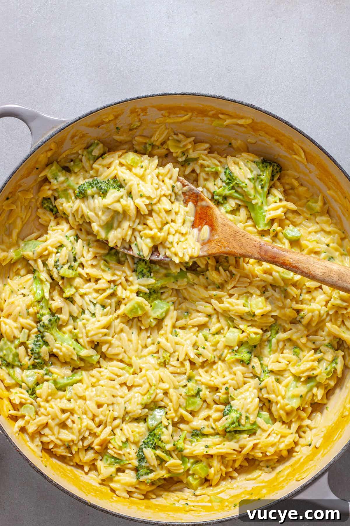 Creamy Broccoli Orzo Pasta with Garlic and Parmesan 12 A wooden spoon pulling out a serving of creamy broccoli orzo with cheddar cheese.