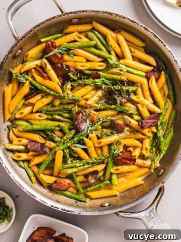 A close-up shot of a skillet with bacon and asparagus pasta garnished with fresh tarragon.
