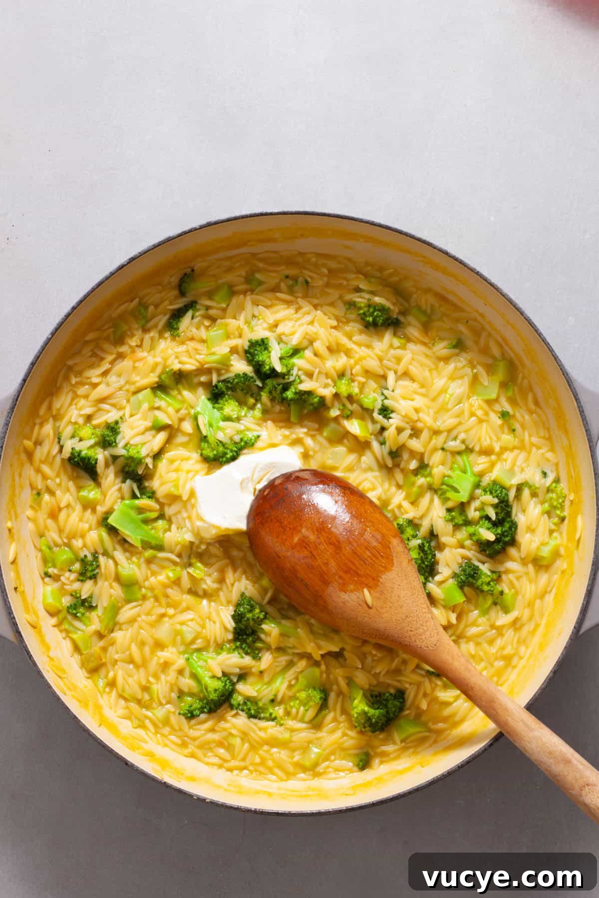 Creamy Broccoli Orzo Pasta with Garlic and Parmesan 9 Cream cheese getting stirred into a large skillet with broccoli and orzo.
