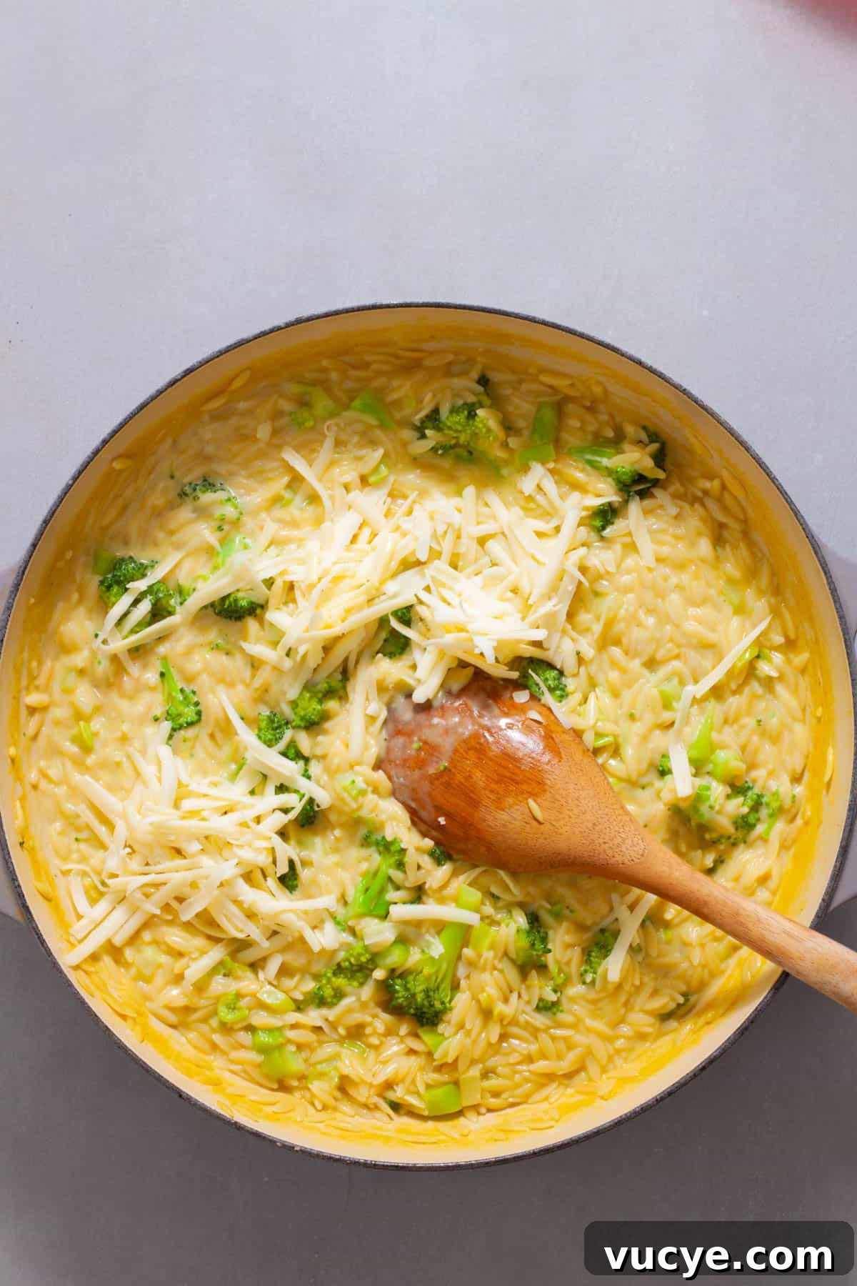 Creamy Broccoli Orzo Pasta with Garlic and Parmesan 10 Shredded cheddar cheese getting stirred into a large skillet with broccoli orzo.