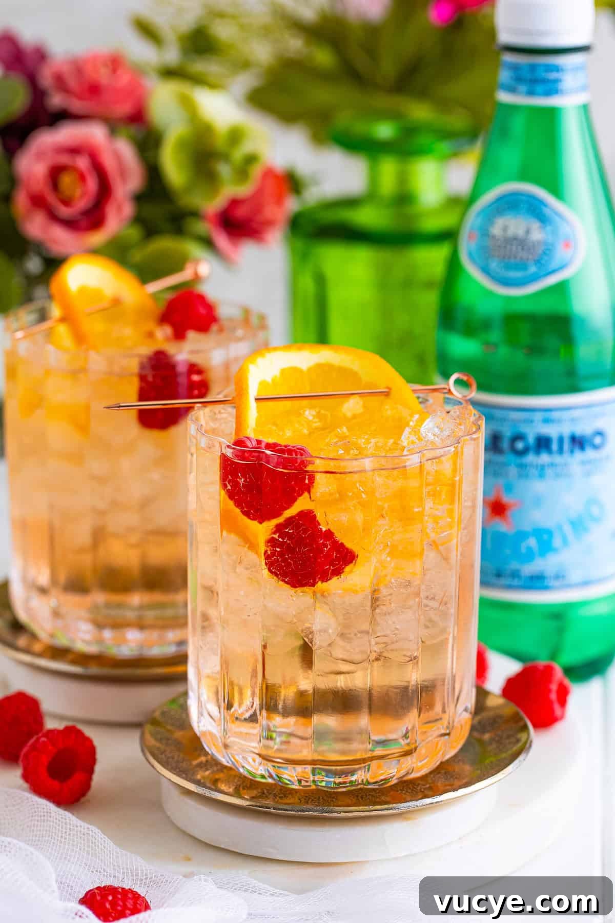 A wine spritzer over ice garnished with an orange slice and raspberries.