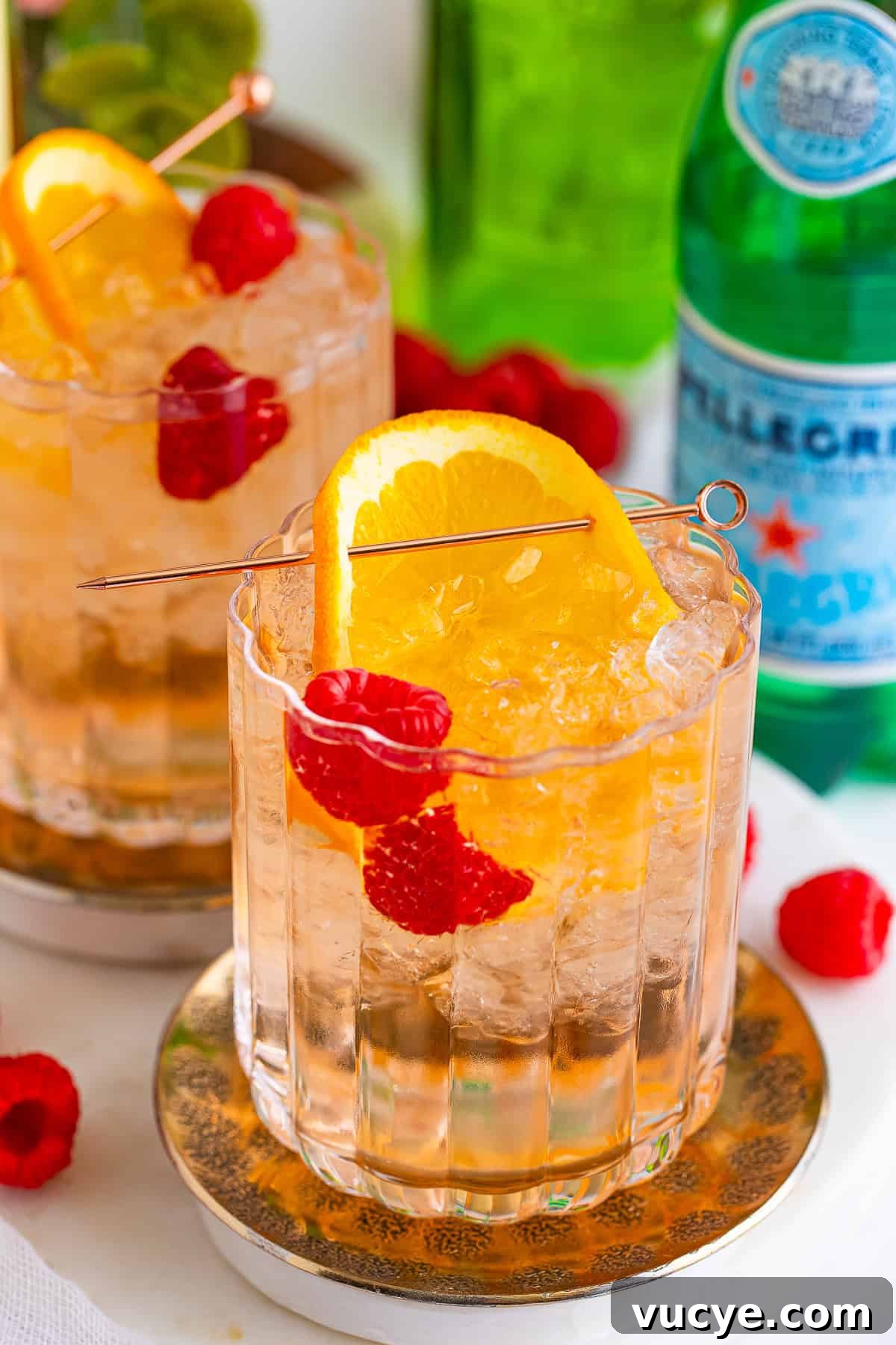 A finished wine spritzer garnished with an orange slice and raspberries.