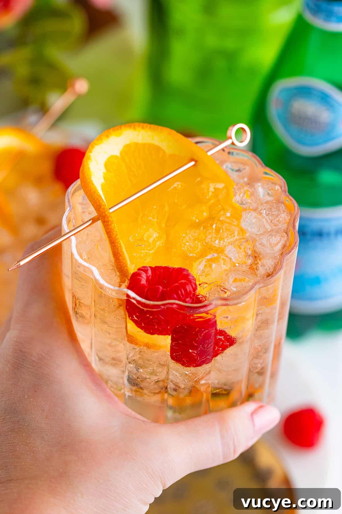 A hand holding a refreshing wine spritzer garnished with orange and raspberries.