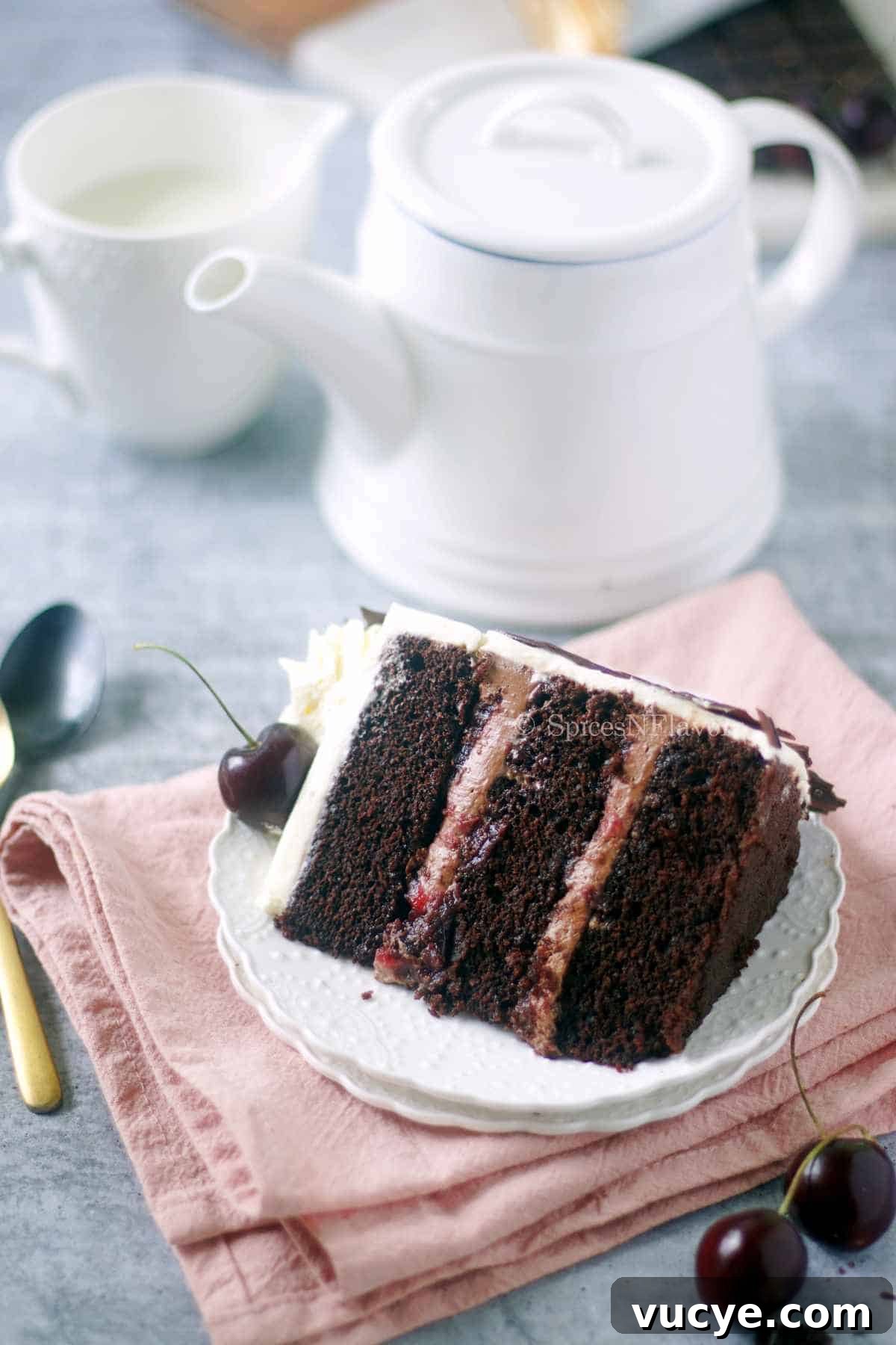 Egg-Free Black Forest Cake Recipe: Rich Chocolate Cherry Dessert 10 sliced piece of cake placed on a white saucer with tea mugs in the background