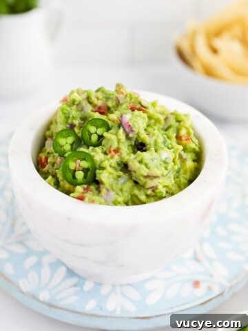 A white marble bowl filled with fresh, bright green guacamole, garnished with three jalapeno slices.
