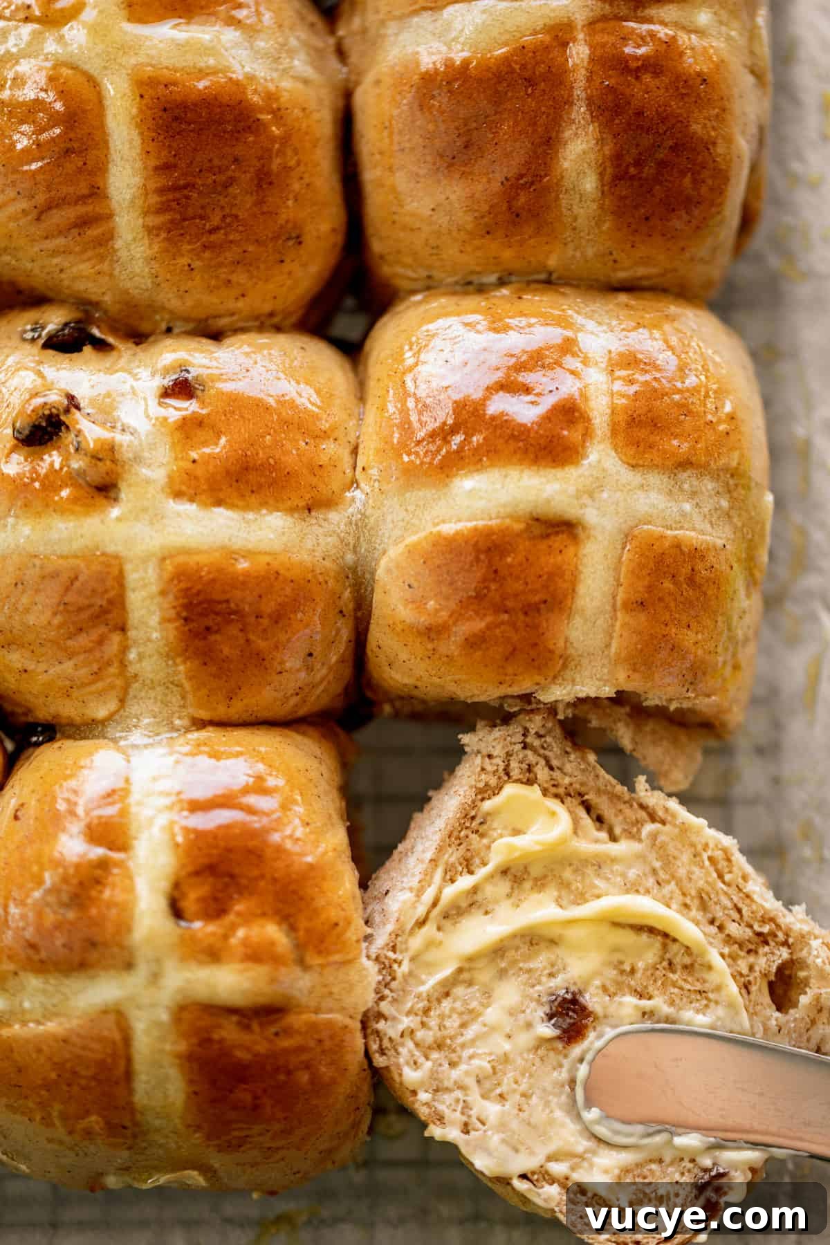 Hot and fluffy Hot Cross Buns with one cut in half and smeared with fresh butter.