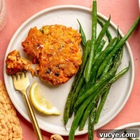 Maple Teriyaki Salmon Rice Bowls with Sesame & Scallions 5 A salmon cake on a plate next to a lemon wedge and a serving of sauteed green beans.