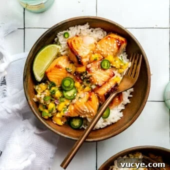 Maple Teriyaki Salmon Rice Bowls with Sesame & Scallions 9 White rice, teriyaki salmon, and mango salsa in a brown bowl sitting on a white tiled table next to a bottle of sparkling water and a white dish towel.