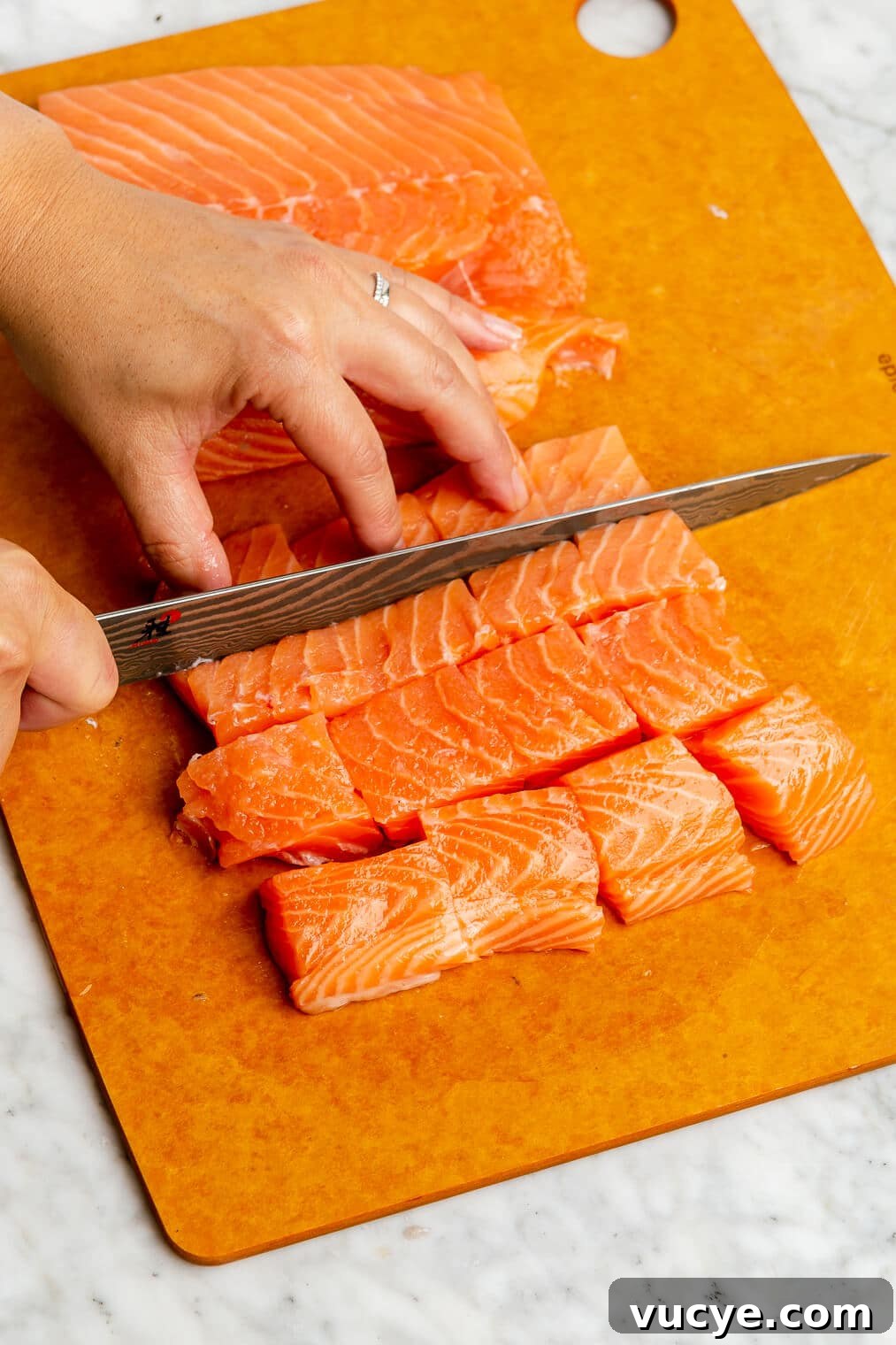 221207_Teriyaki Salmon Bowls-03 A salmon filet being cut into cubes on an orange cutting board.