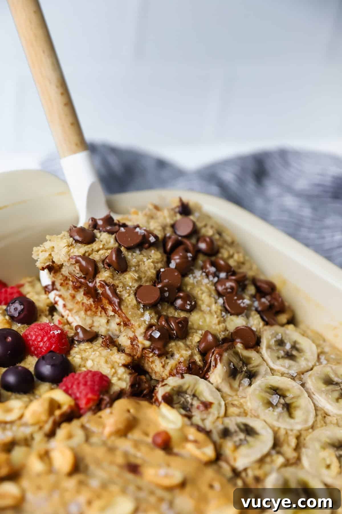 Chewy Baked Oatmeal Casserole with Berries and Cinnamon 5 A delicious baked oatmeal, bursting with chocolate chips, sliced bananas, berries, and nuts. A spatula gracefully lifts a portion of this comforting dish.