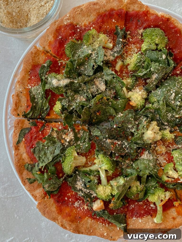 Paleo Pizza Crust Without Yeast: Quick Grain-Free Recipe 2 paleo pizza with broccoli and kale on a white plate with small bowl of vegan parmesan