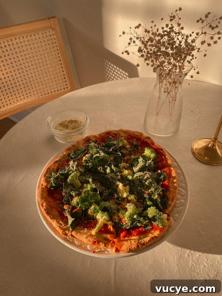 Paleo Pizza Crust Without Yeast: Quick Grain-Free Recipe 3 paleo pizza with broccoli and kale on a white plate with small bowl of vegan parmesan and vase with white flowers