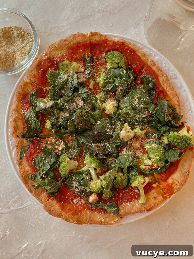 Paleo Pizza Crust Without Yeast: Quick Grain-Free Recipe 4 paleo pizza with broccoli and kale on a white plate with small bowl of vegan parmesan