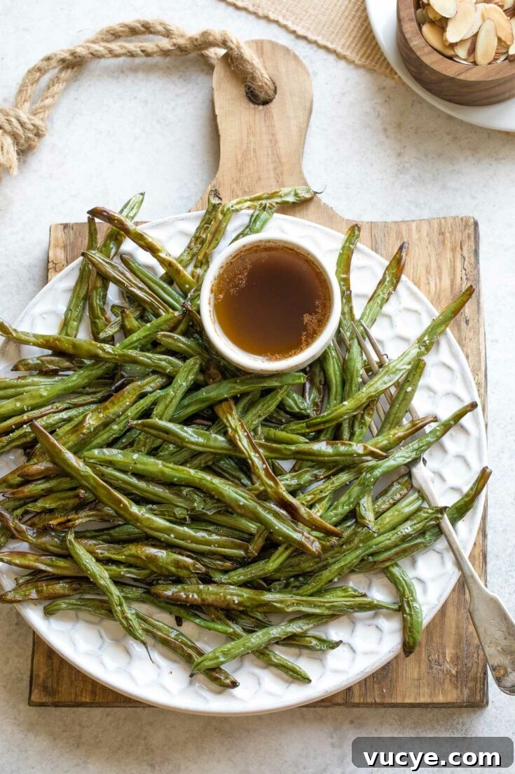 Platter of air-fried green beans with a bowl of sauce and almonds nearby.