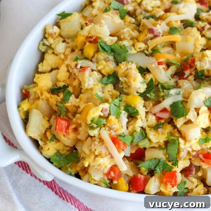 Closeup of oval serving bowlful of breakfast scramble on white cloth with thin red stripe.