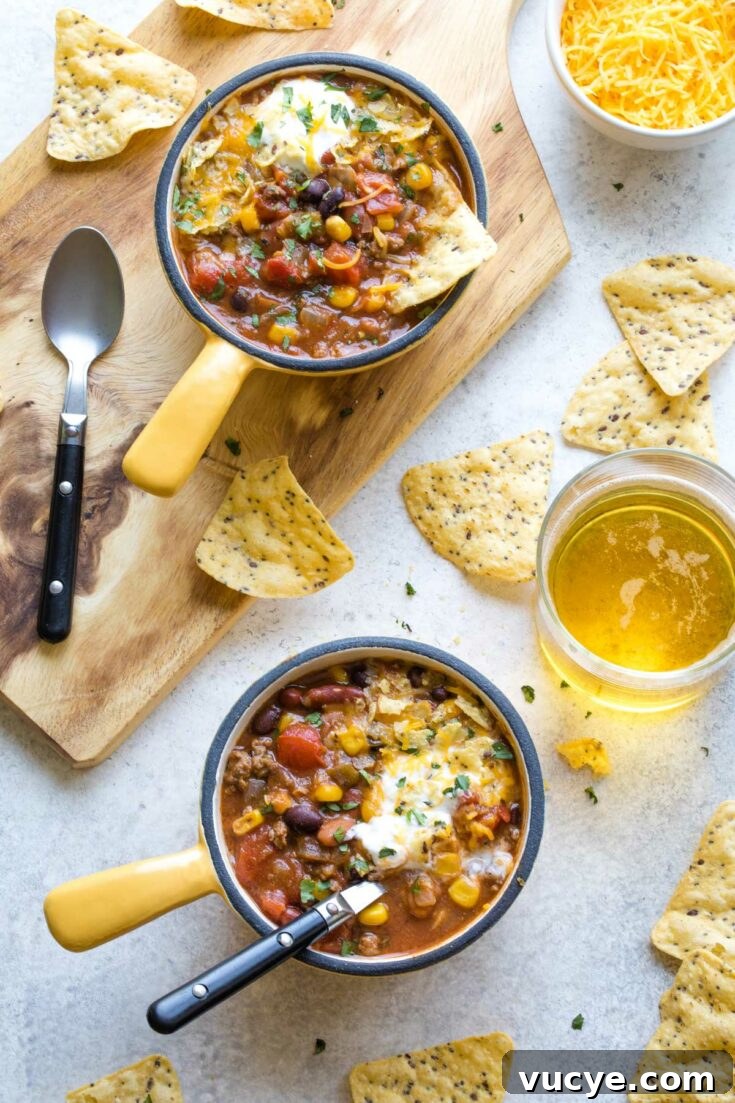 Two bowls of hearty taco soup with tortilla chips and shredded cheese nearby.