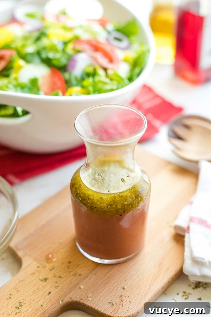 Bottle of red wine vinaigrette beside a salad on a wooden board.