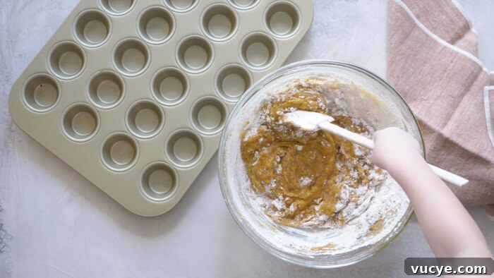 toddler helping stir pumpkin puree into muffin batter