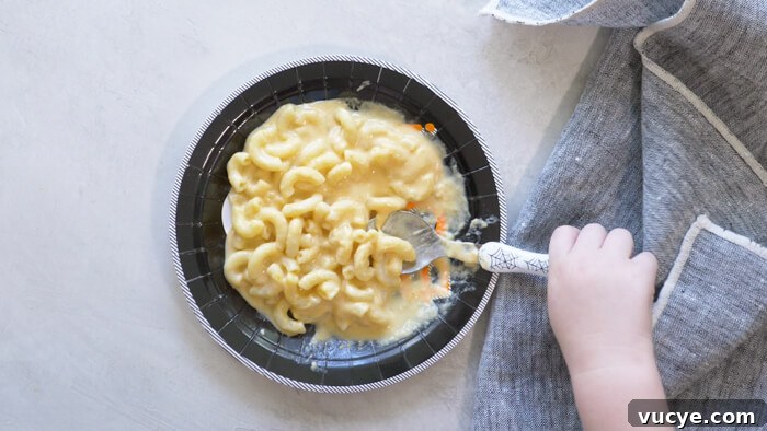 toddler hand eating pumpkin mac n cheese