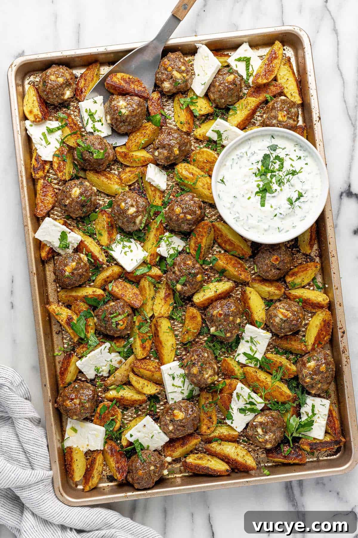 Greek-Style Sheet Pan Meatballs with Roasted Potatoes 2 Sheet pan with meatballs, roasted potatoes, sliced feta, and fresh herbs.