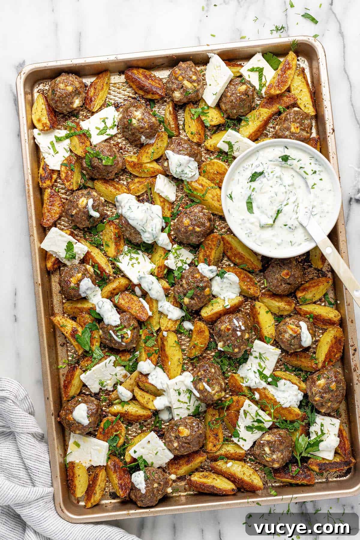 Greek-Style Sheet Pan Meatballs with Roasted Potatoes 9 Sheet pan with meatballs, roasted potatoes, sliced feta, and fresh herbs.
