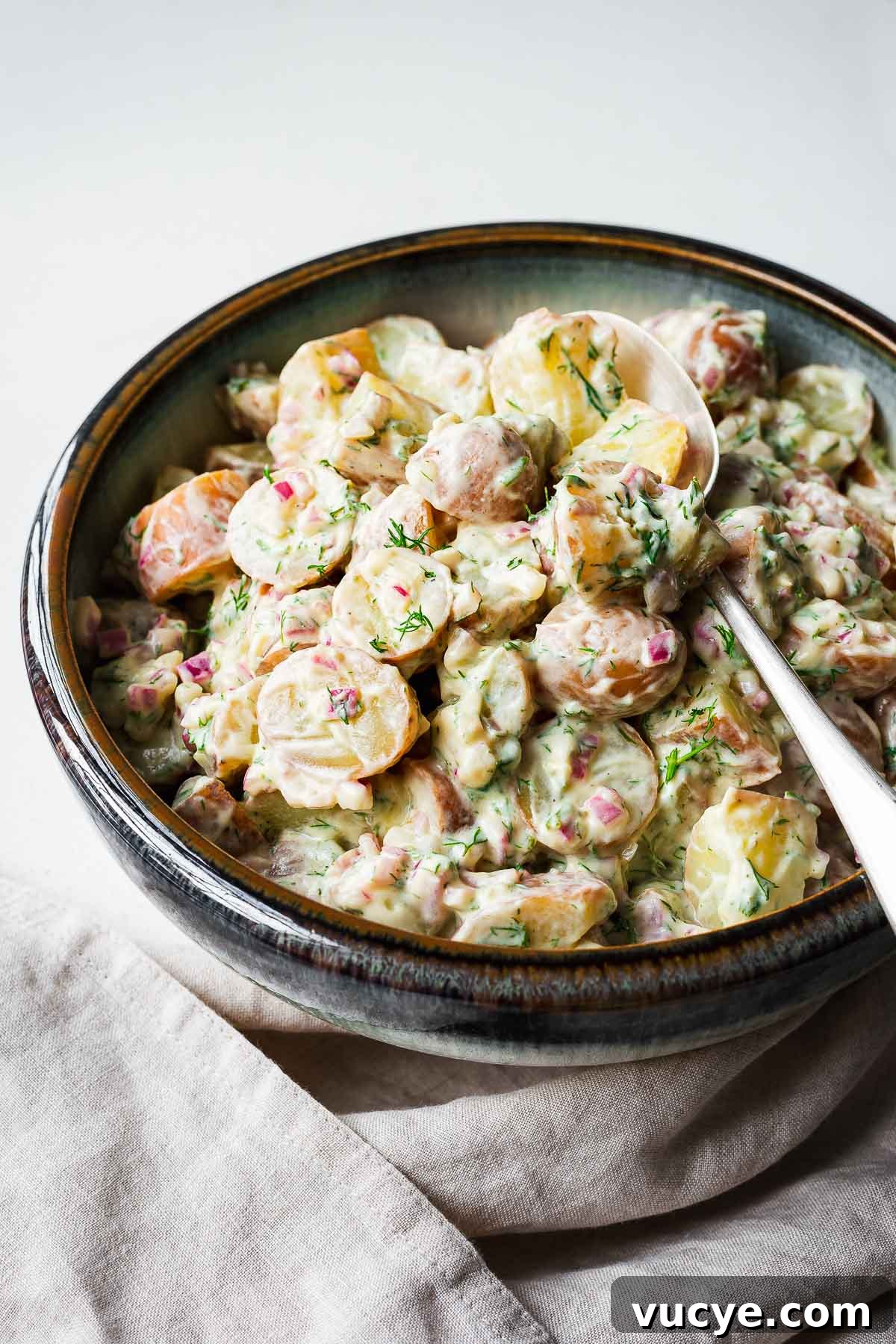 Red potato salad with dill and a creamy dressing in a serving bowl with silver spoon.