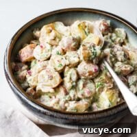 Red potato salad with dill and a creamy dressing in a serving bowl with silver spoon.