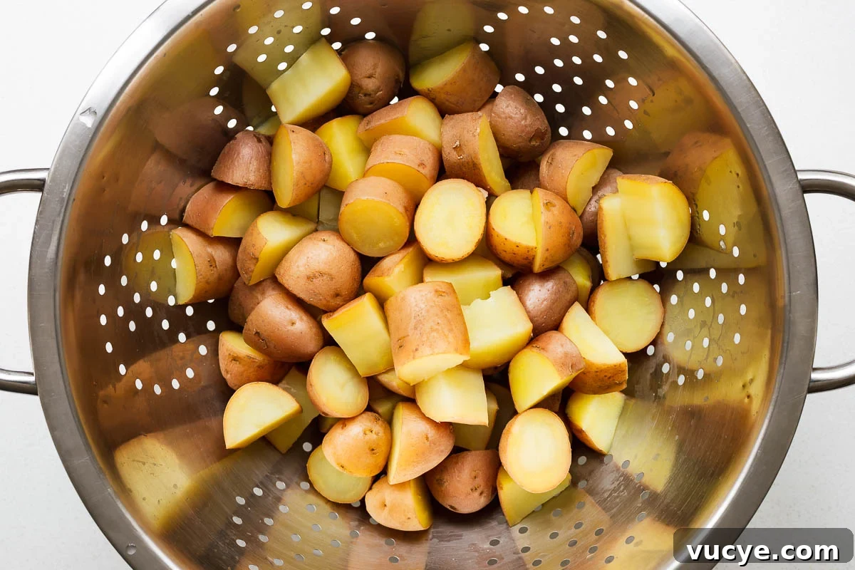 Cooked cut red potatoes straining in a colander viewed from above.
