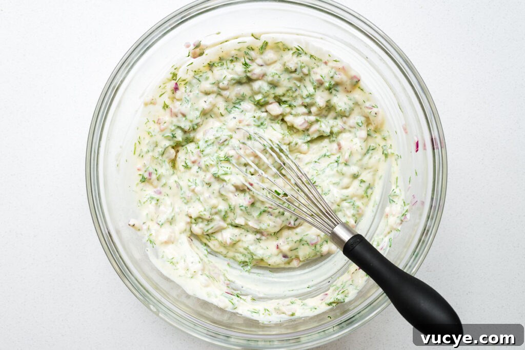 Creamy dill dressing for potato salad in a large mixing bowl with a wire whisk.