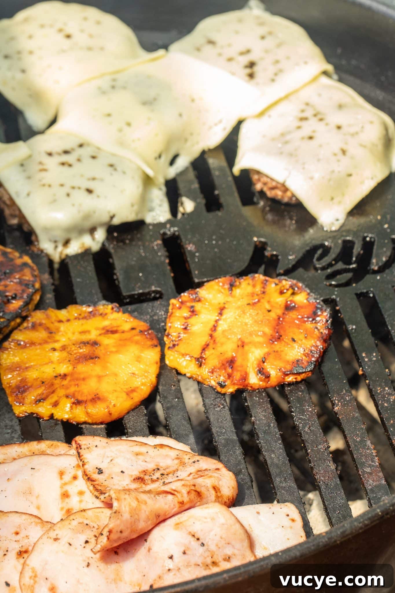 grilling a pineapple teriyaki burger Cheese topped burger patties on the grill with grilled pineapple and ham