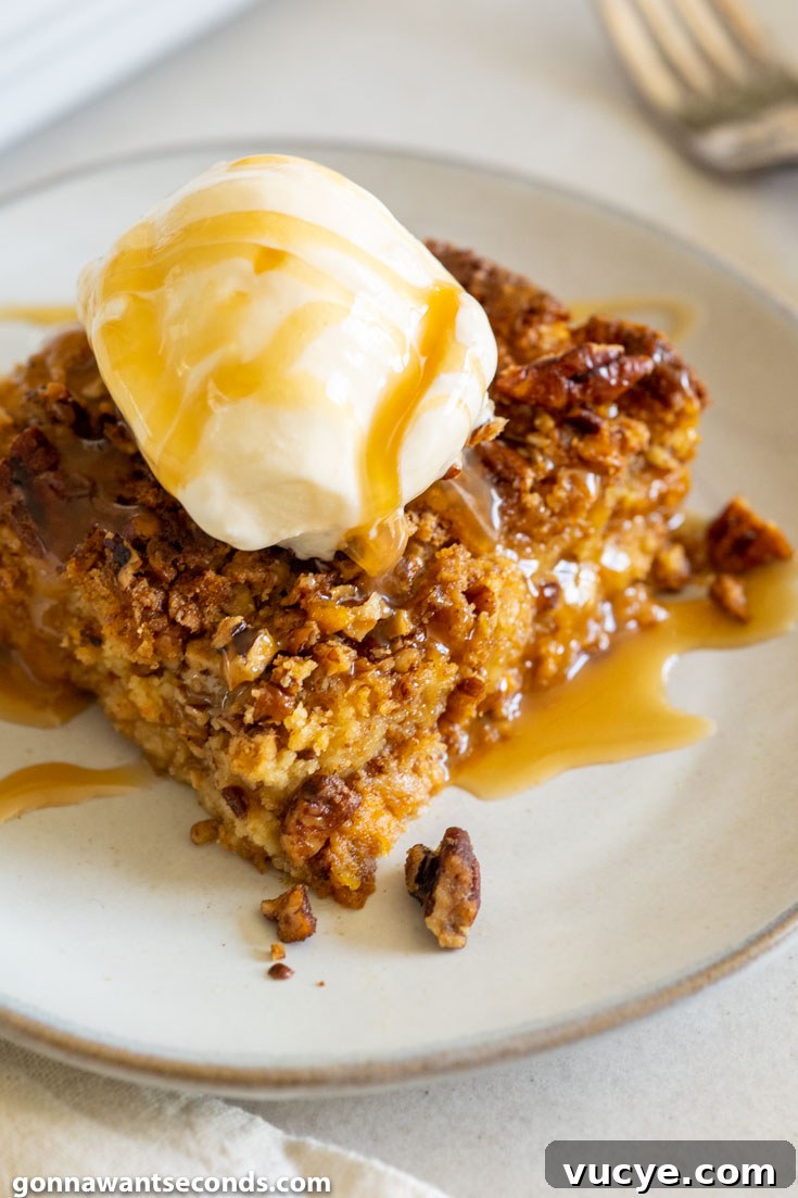A slice of pumpkin dump cake with evaporated milk, topped with vanilla ice cream and drizzled with caramel