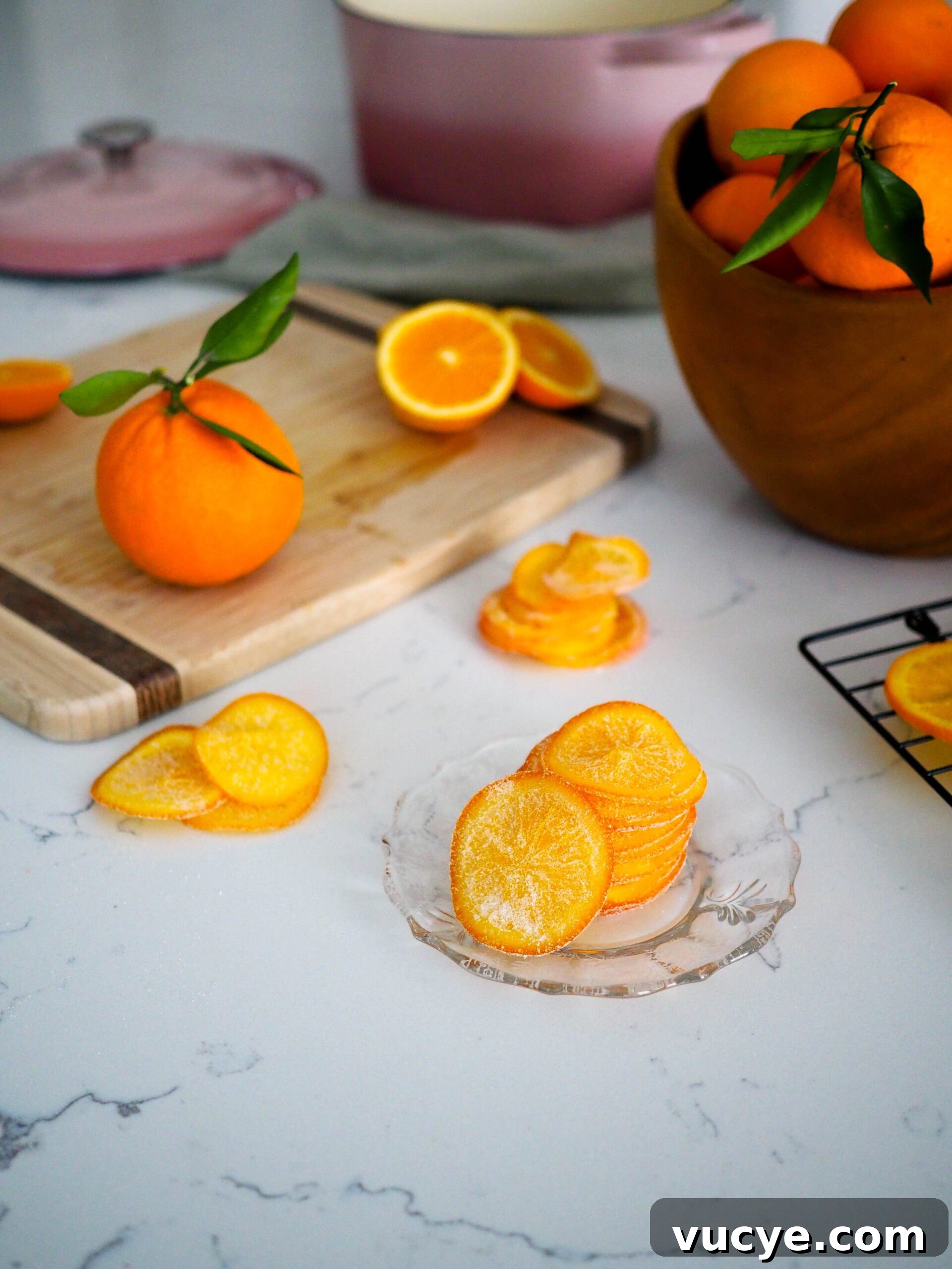 Candied Orange Slices Recipe: How to Make Sweet Orange Candy 2 A stack of candied orange slices on a glass plate with styled oranges around it.