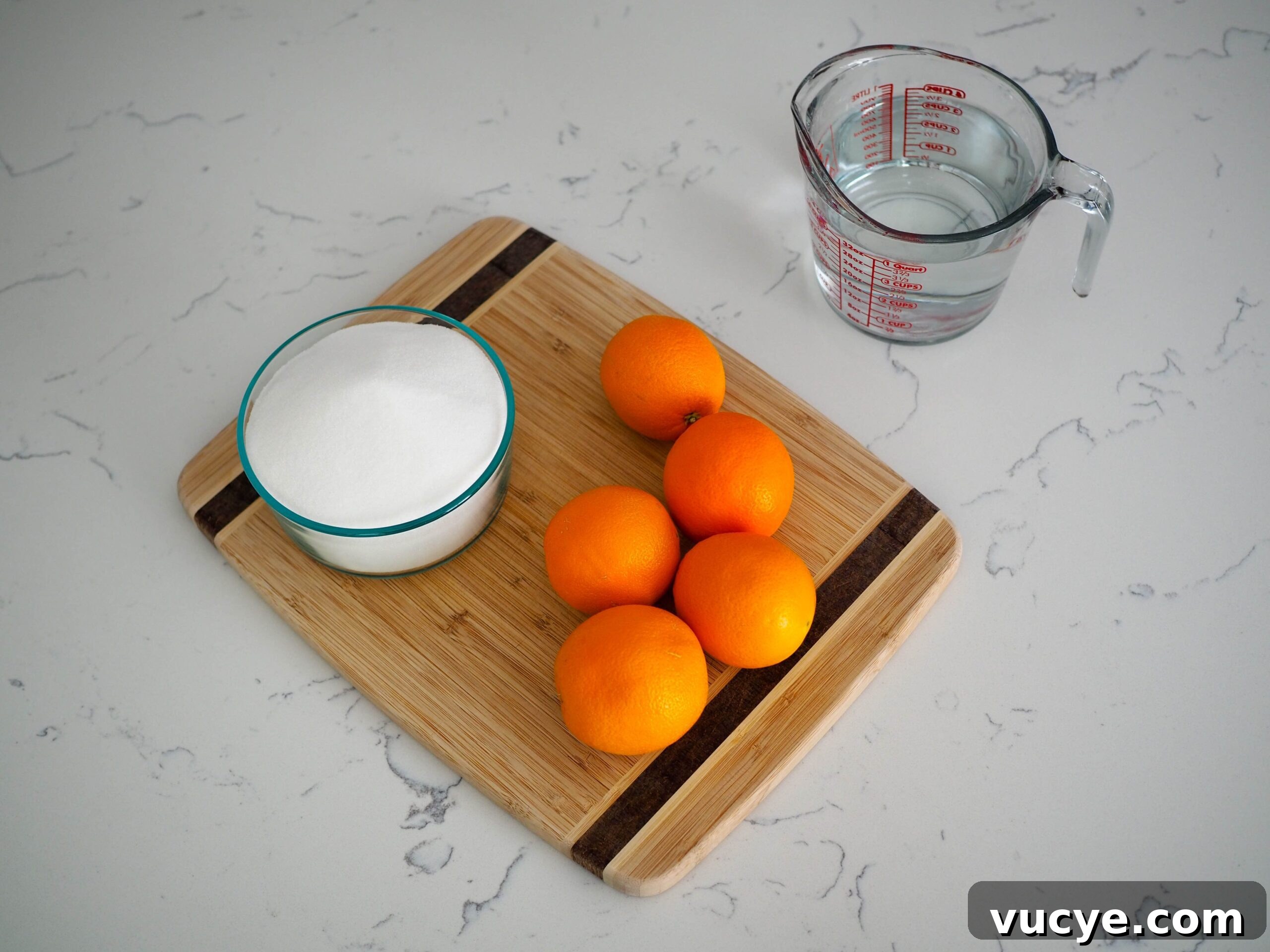 Candied Orange Slices Recipe: How to Make Sweet Orange Candy 3 Five oranges, a bowl of sugar, and water on a quartz counter.