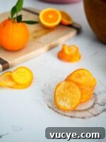 Candied Orange Slices Recipe: How to Make Sweet Orange Candy 8 A stack of candied orange slices on a glass plate, with a bowl of oranges in the background.