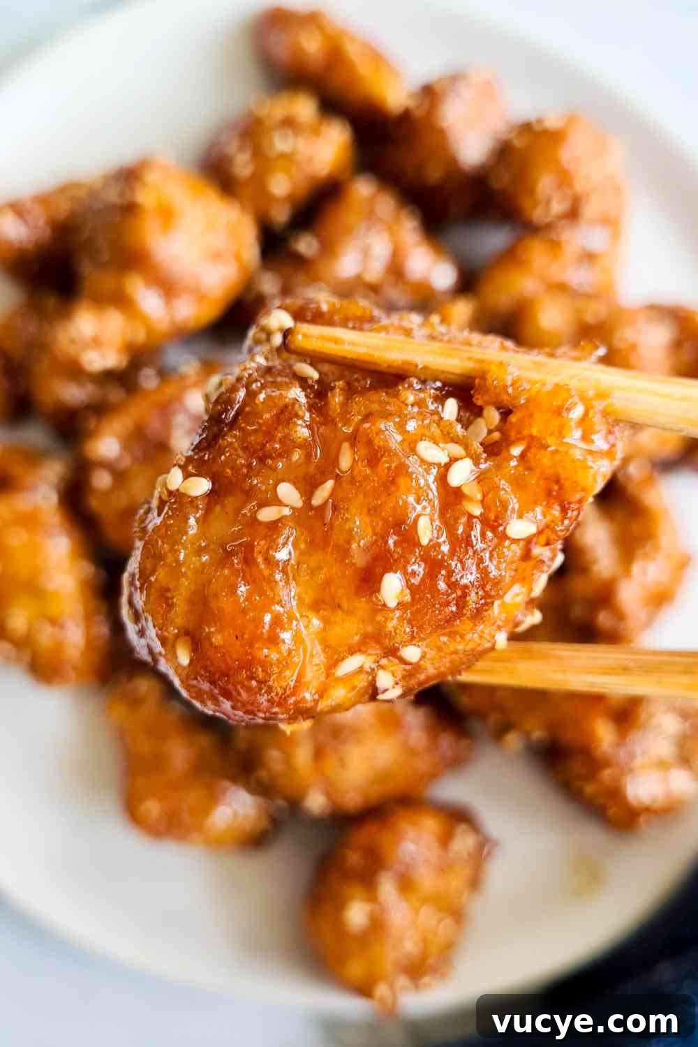 A piece of crispy chicken bite being held up of a pair of chopsticks