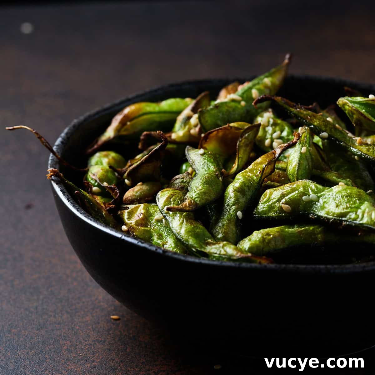 Crispy Air Fryer Frozen Edamame in 10 Minutes 10 Photo of a black bowl filled with air fryer frozen edamame beans set on a rusted black surface.