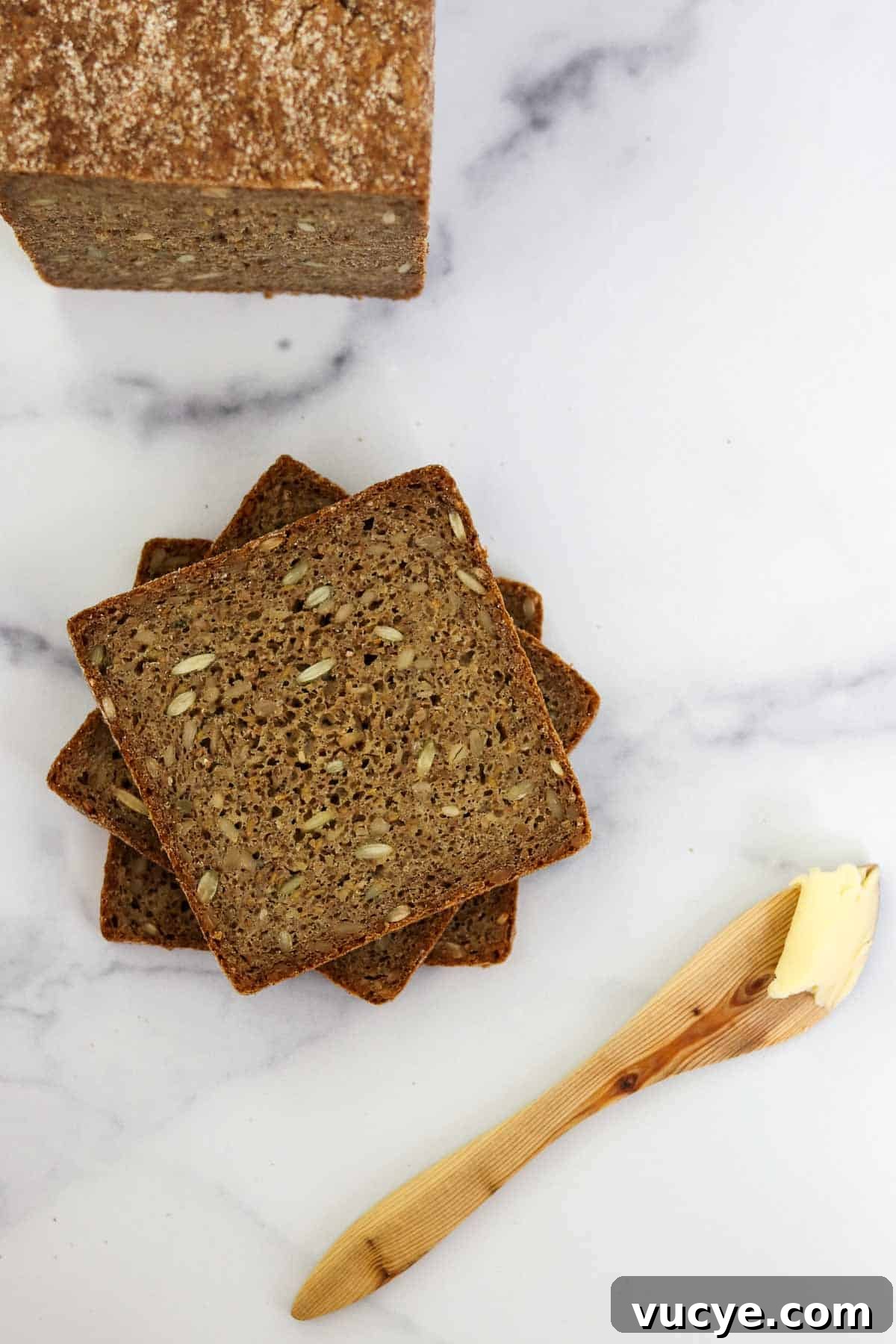 Slices of rye bread stacked on a marble surface next to a wooden butter knife.