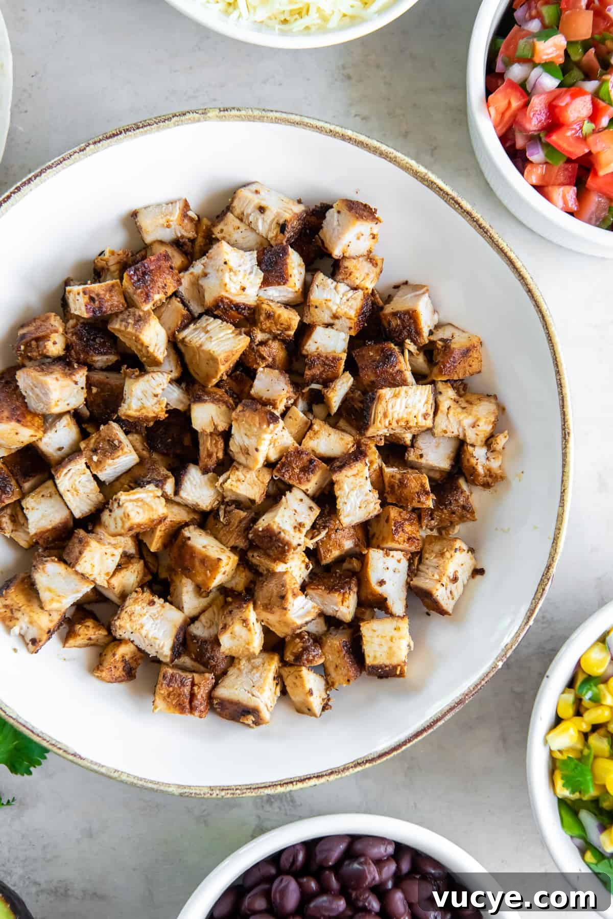 Smoky Chipotle Chicken Recipe: Juicy Grilled Chicken with Sauce 3 A top down shot of copycat Chipotle chicken in a white bowl surrounded by other ingredients in bowls.