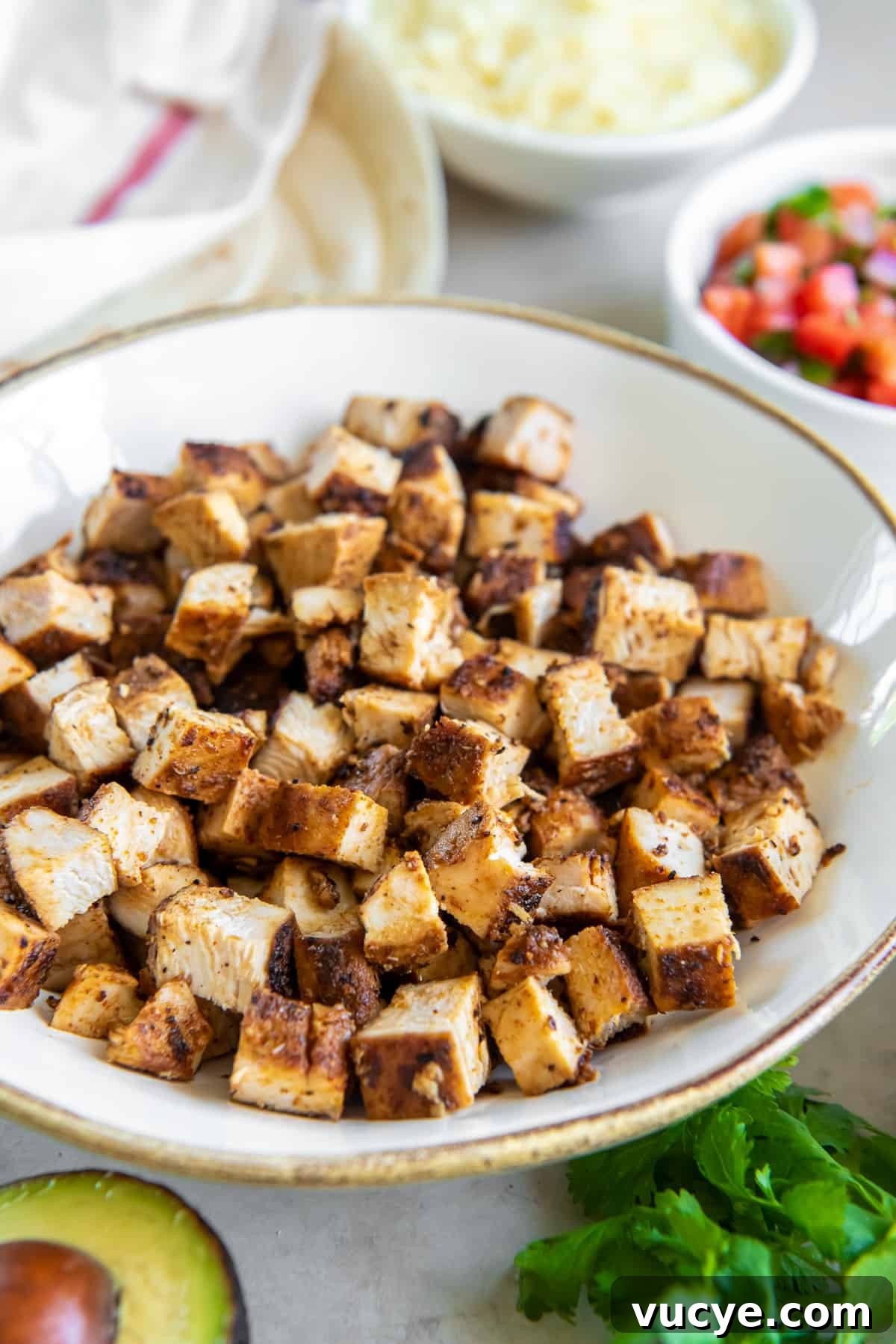 Smoky Chipotle Chicken Recipe: Juicy Grilled Chicken with Sauce 7 A side view of cubed copycat Chipotle chicken in a white bowl surrounded by ingredients in smaller bowls.