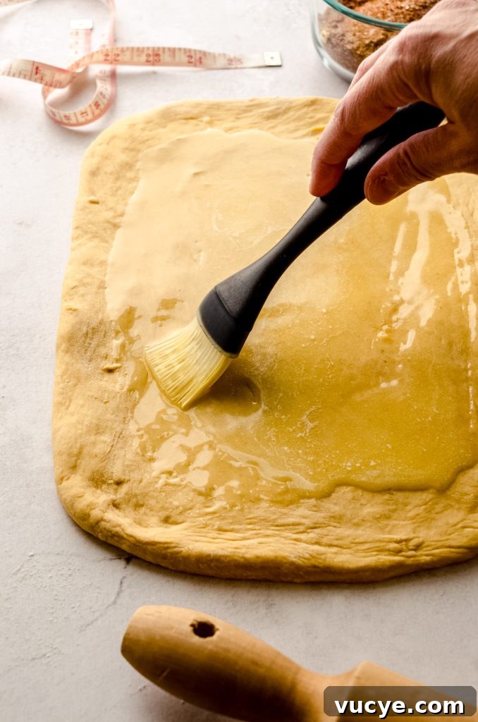 Someone is brushing melted butter onto a rectangle of dough to make pumpkin cinnamon rolls.