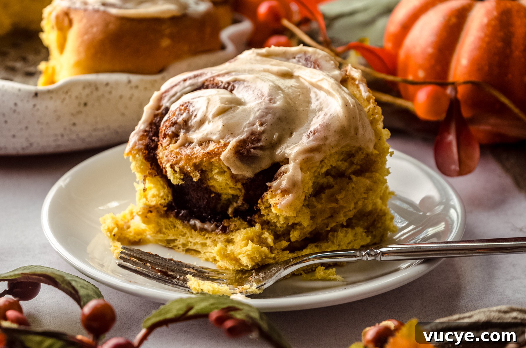 A pumpkin cinnamon roll on a plate with a fork and a bite taken out of it.