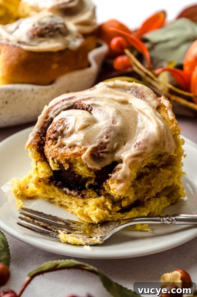 A pumpkin cinnamon roll on a plate with a fork and a bite taken out of it.