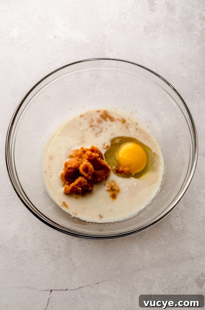 An egg, pumpkin, and wet ingredients in a large glass bowl to make pumpkin cinnamon rolls.