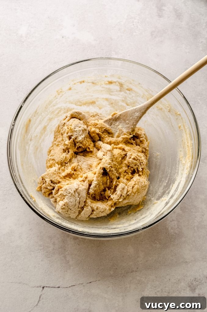 A progress photo of the ingredients make pumpkin cinnamon rolls being mixed in a large bowl with a wooden spoon.