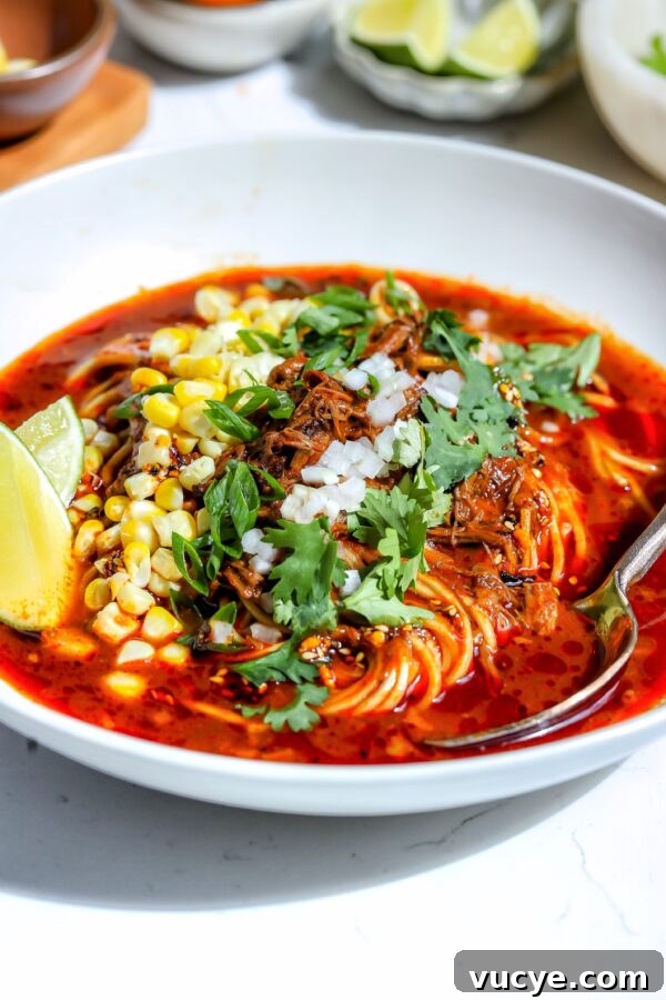 A vibrant bowl of birria ramen with shredded meat and garnishes.