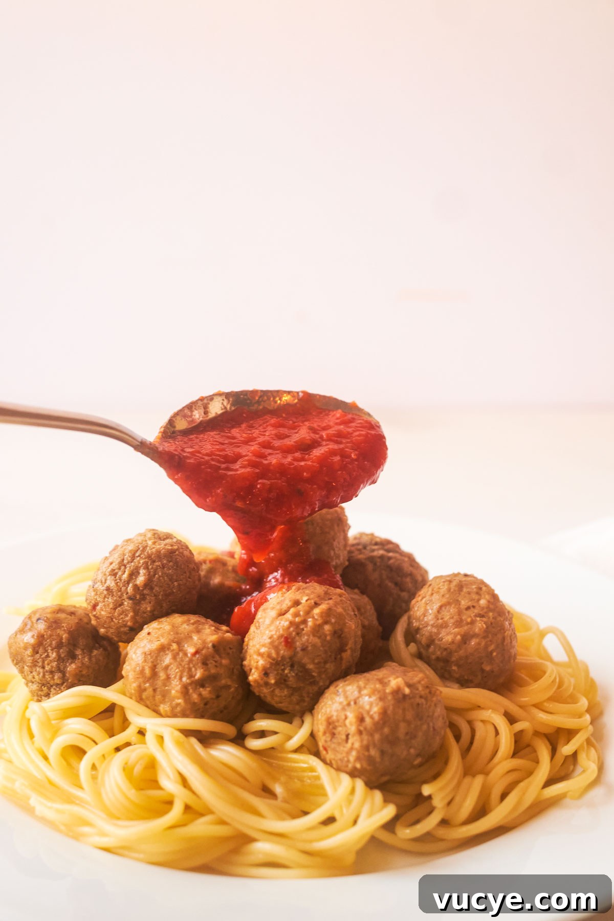a spoon pouring sauce over cooked frozen meatballs and pasta