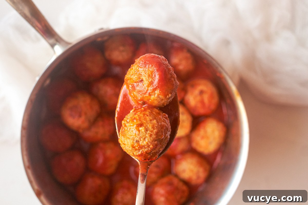 top down view of a spoon removing two cooked frozen meatballs from a saucepan