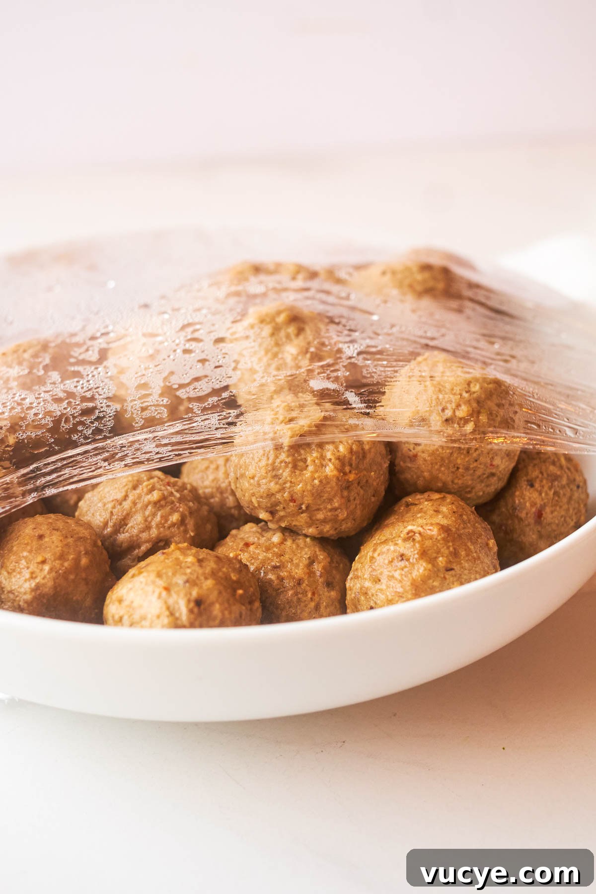 frozen meatballs in a dish covered with plastic wrap to show how to cook frozen meatballs in microwave