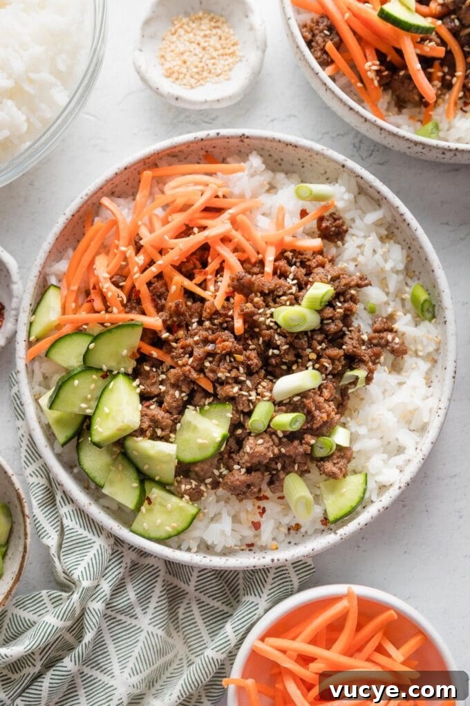 Ceramic bowl full of Korean-inspired ground beef and rice served with cucumber, shredded carrot, and toasted sesame seeds.